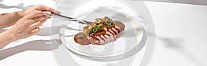 Young woman eat roasted duck breast with fork and knife. Female hand cuts duck fillet. Hands with knife and fork in trendy menu