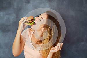 Young woman eating appetizing hamburger greedily
