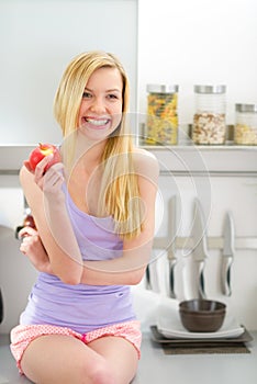 Young woman eating apple in kitchen