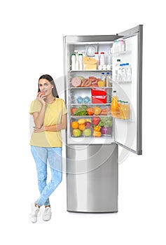 Young woman eating apple near open refrigerator