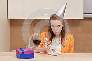 Young woman eating birthday cake. On the head of a festive cap of silver color.