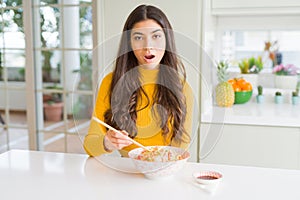 Young woman eating a bowl of Asian rice using chopsticks scared in shock with a surprise face, afraid and excited with fear