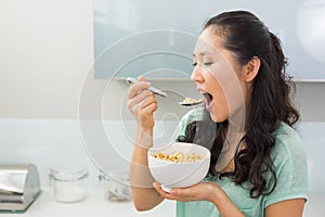 Young woman eating cereals in kitchen