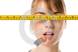 young woman eating cherry tomato with measuring tape in front her eyes