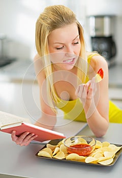 Young woman eating chips and reading book