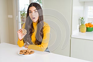 Young woman eating chocolate chips cookies at home scared in shock with a surprise face, afraid and excited with fear expression