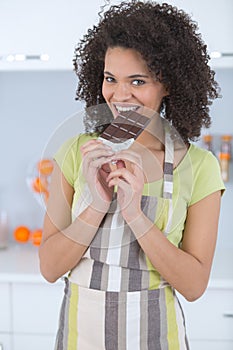 Young woman eating chocolate on light background