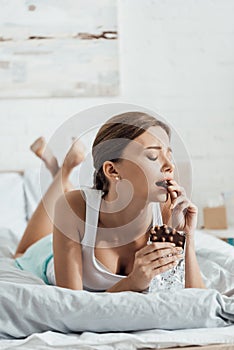 Young woman eating chocolate with nuts in bed
