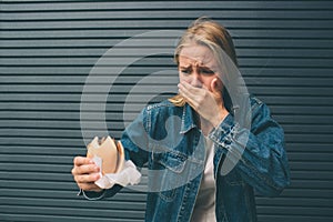 Young woman eating fast food outdoor and feels very bad