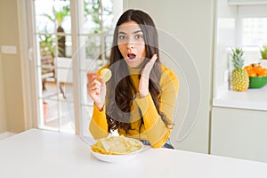 Young woman eating fastfood potato chips scared in shock with a surprise face, afraid and excited with fear expression