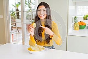 Young woman eating fastfood potato chips very happy pointing with hand and finger