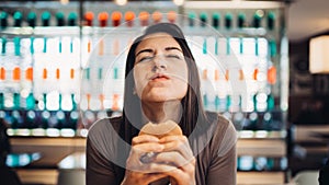 Young woman eating fatty hamburger.Craving fast food.Enjoying guilty pleasure,eating junk food.Satisfied expression.Breaking diet