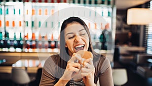 Young woman eating fatty hamburger.Craving fast food.Enjoying guilty pleasure,eating junk food.Satisfied expression.Breaking diet