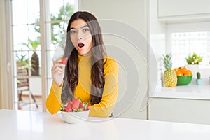 Young woman eating fresh red strawberry as healthy snack scared in shock with a surprise face, afraid and excited with fear