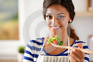 Young woman eating fresh salad in modern kitchen