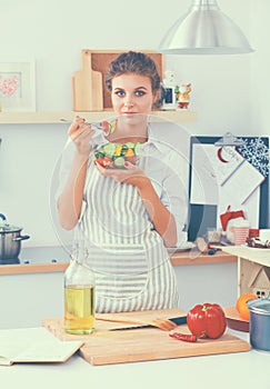 Young woman eating fresh salad in modern kitchen