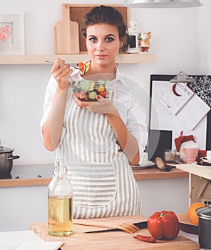 Young woman eating fresh salad in modern kitchen