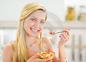 Young woman eating fruits salad in kitchen