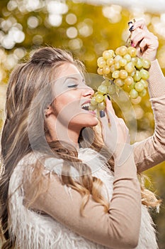 Young woman eating grapes outdoor. Sensual blonde female smiling holding a bunch of green grapes. Beautiful fair hair girl