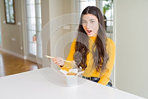 Young woman eating noodles in delivery box scared in shock with a surprise face, afraid and excited with fear expression