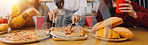 Young woman eating pizza and laughing while sitting with her friends in a restaurant. Group of friends enjoying while having food