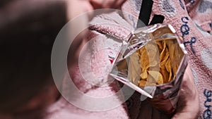 Young Woman Eating Potato Chips From a Bag of Chips on Couch at Home Close-Up