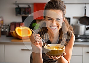 Young woman eating pumpkin soup in kitchen