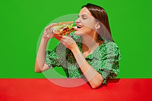 Young woman eating quirky sandwich with doll against red background. Weirdness and surrealism.