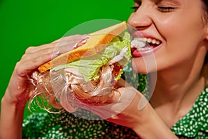 Young woman eating quirky sandwich with doll against red background. Weirdness and surrealism.