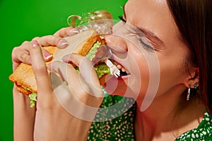 Young woman eating quirky sandwich with doll against red background. Weirdness and surrealism. Close-up