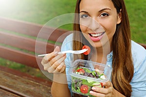 Young woman eating salad on lunch break in city park living healthy lifestyle. Happy smiling brazilian girl eating outdoor