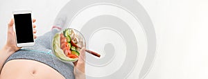 Young woman is eating a salad and using a fitness app on her smartphone after a workout.