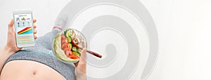 Young woman is eating a salad and using a fitness app on her smartphone after a workout.