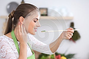 Young woman eating salad by wooden spoon while cooking in a kitchen. Healthy meal, food and kitchen work concept