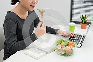 Young woman eating salad while working at desk. Weight loss concept