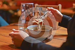 Young woman eating soup served in a white bowl. Eating out. Restaurant concept. Woman` s hand holding spoon.