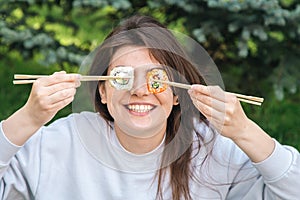 A young woman eating sushi in the park, picnic in nature.