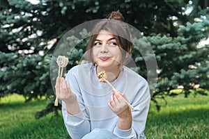 A young woman eating sushi in the park, picnic in nature.