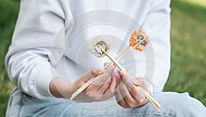 A young woman eating sushi in the park, picnic in nature.