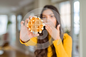 Young woman eating sweet waffle pastry cover mouth with hand shocked with shame for mistake, expression of fear, scared in