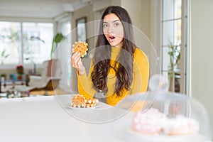 Young woman eating sweet waffle pastry scared in shock with a surprise face, afraid and excited with fear expression