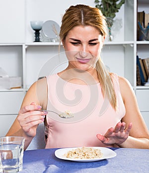 Young woman is eating tasteless oatmeal porridge and feeling disgust