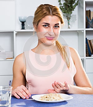 Young woman is eating tasteless oatmeal porridge and feeling disgust