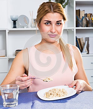 Young woman is eating tasteless oatmeal porridge and feeling disgust