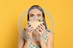 Young woman eating tasty sandwich on background