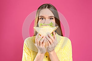 Young woman eating tasty sandwich on background