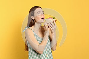 Young woman eating tasty sandwich on background