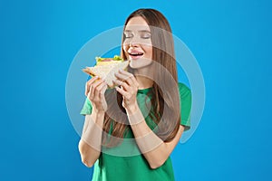 Young woman eating tasty sandwich on blue background