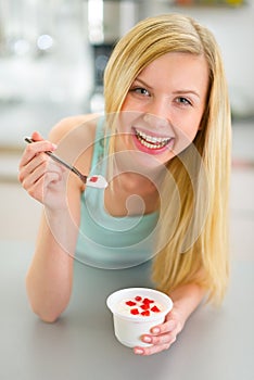 Young woman eating yogurt in kitchen