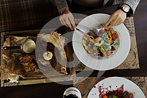 A young woman eats a fresh salad with salmon and a juicy steak and butter at an elegantly laid table in a restaurant.